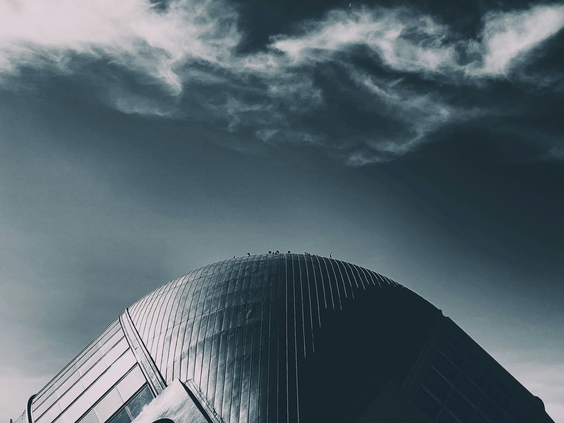 Dark curved building rising into a turbulent blue-grey sky in Valencia